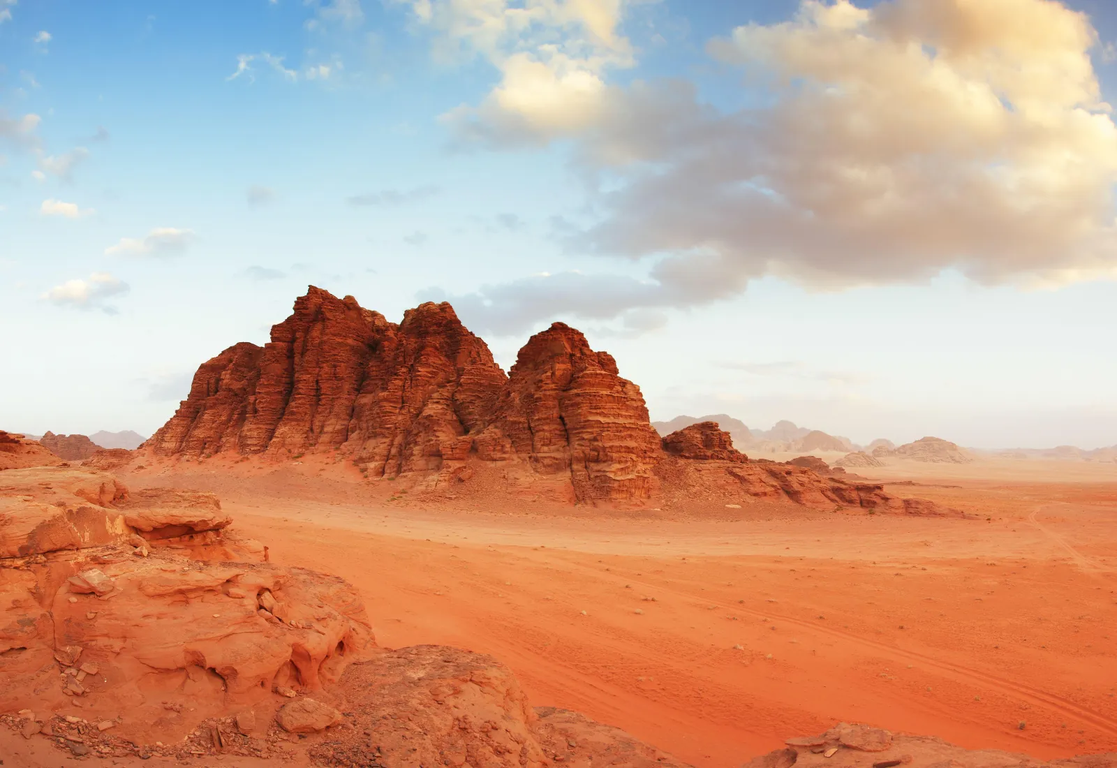 A lone jagged massif rising from flat red sand in Wadi Rum