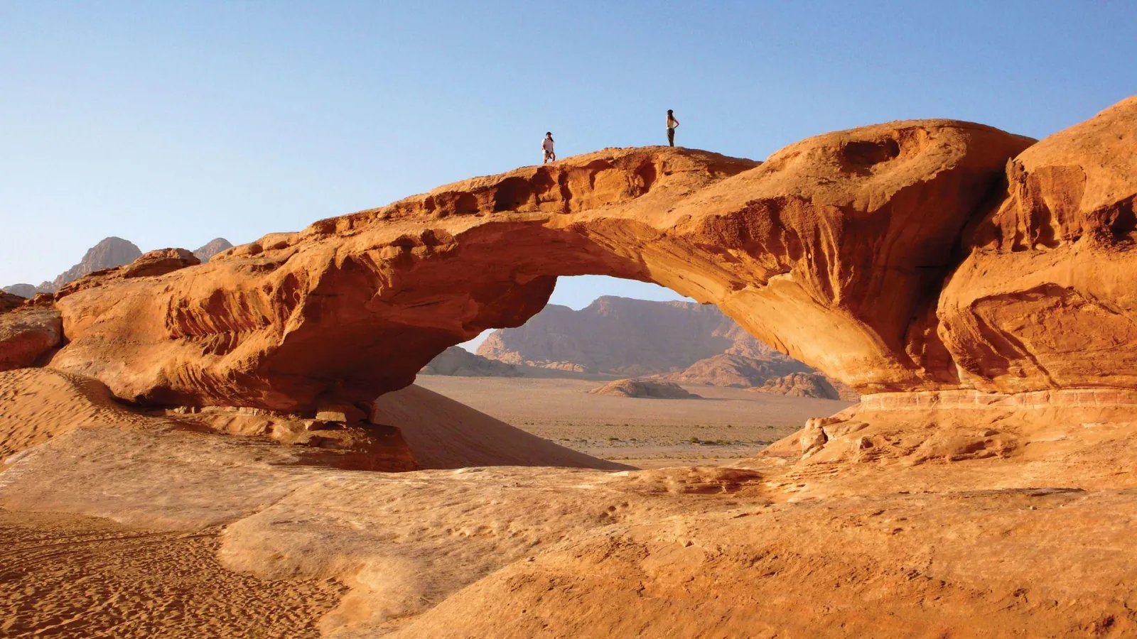 Two figures standing on top of Wadi Rum's Burdah rock bridge