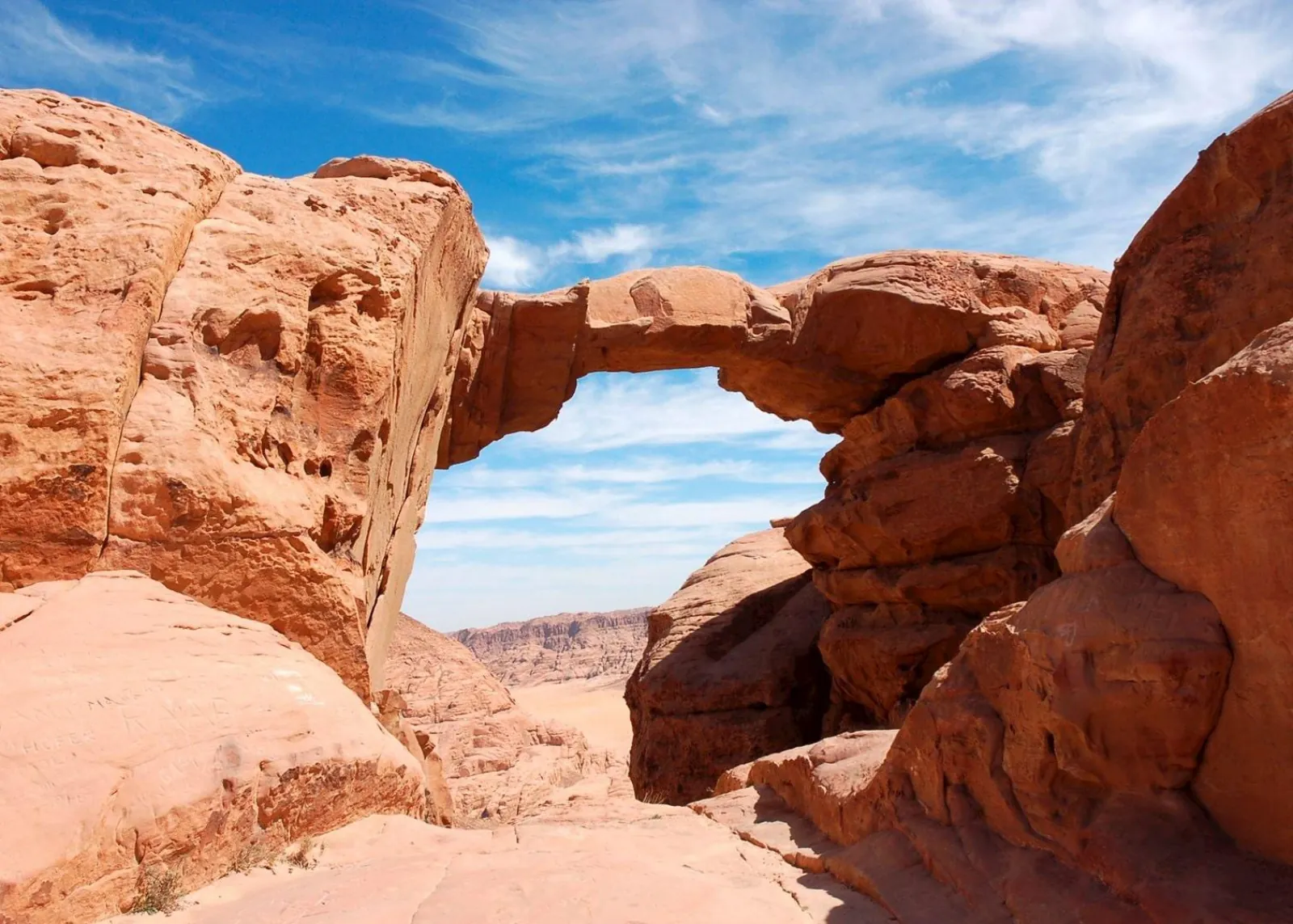 A low natural rock arch spanning sandstone boulders in Wadi Rum
