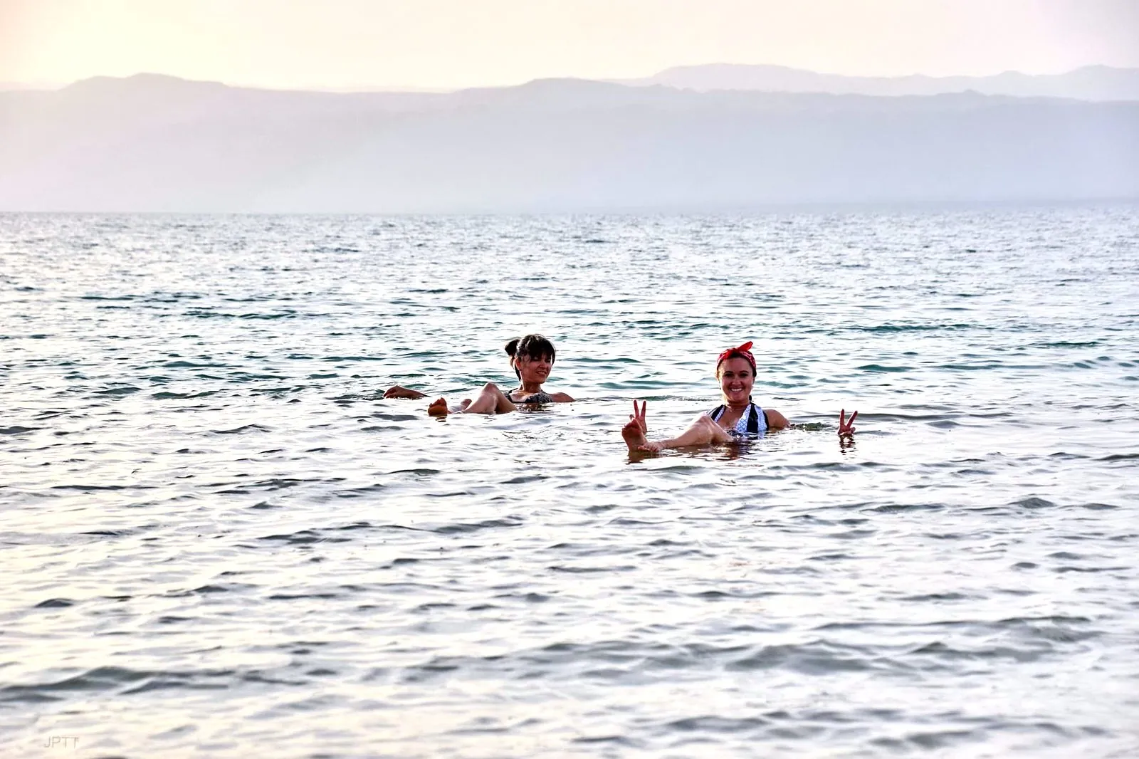 Two swimmers floating upright in the Dead Sea with their hands out of the water