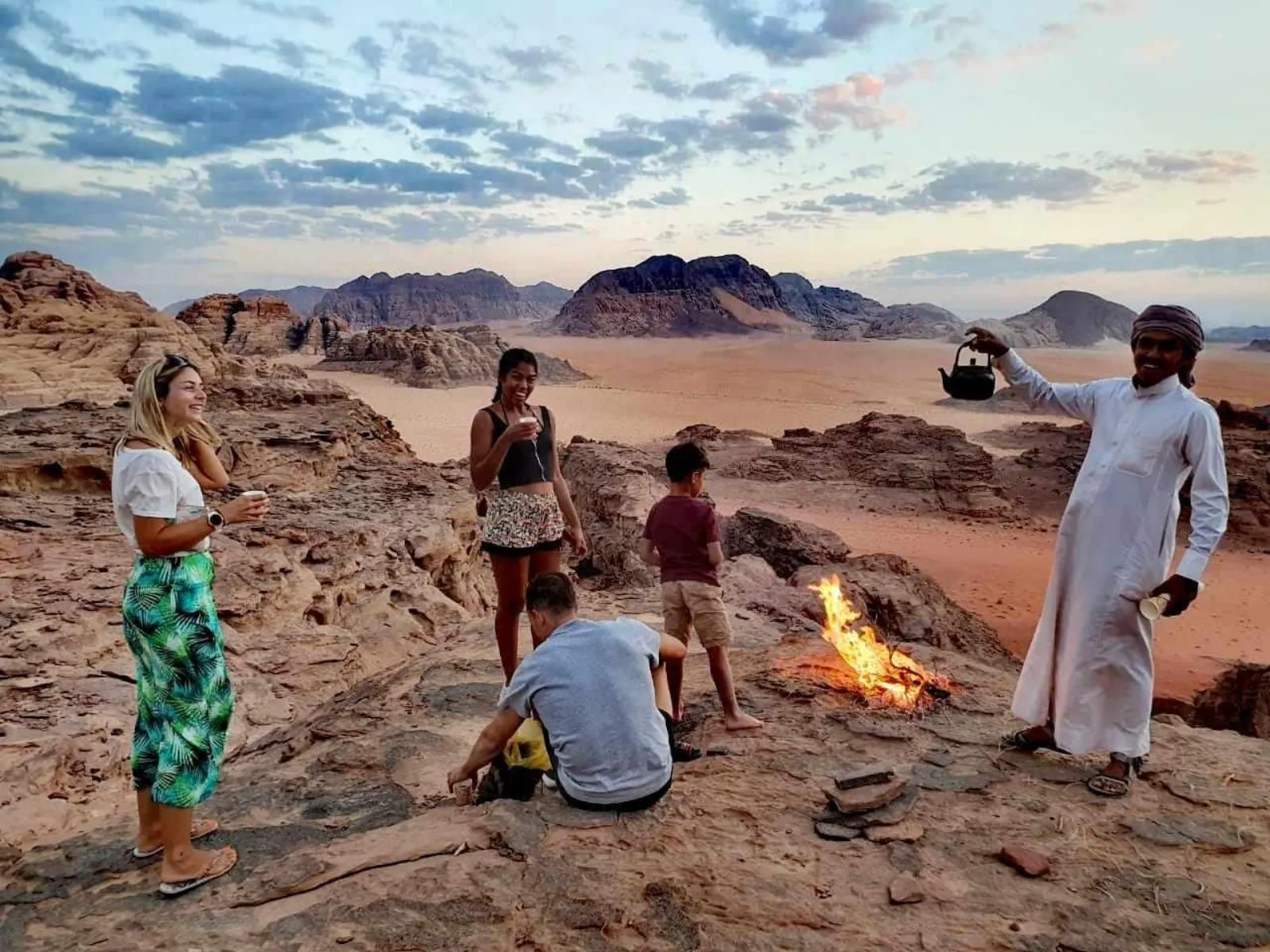 Travellers gathered round a fire on the rocks as the sun drops over Wadi Rum