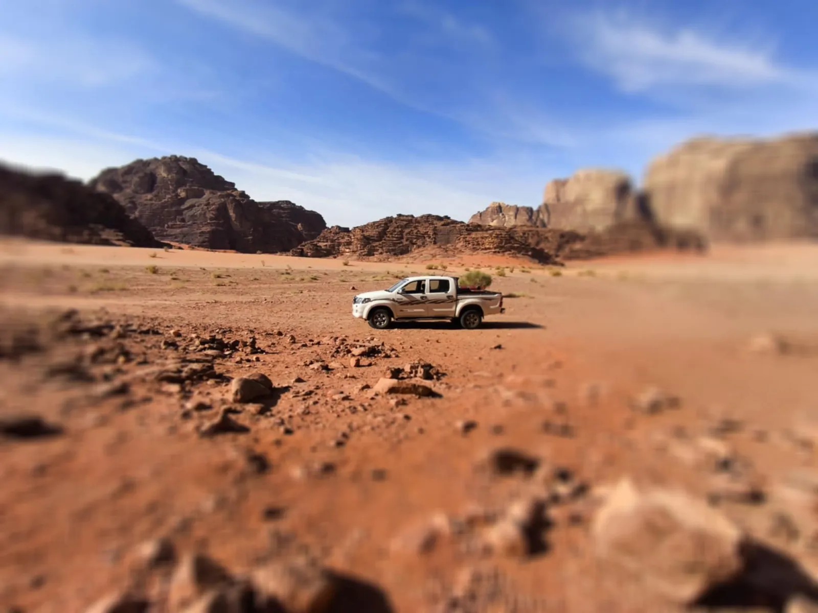 A white pickup parked alone on the desert floor beneath Wadi Rum's cliffs