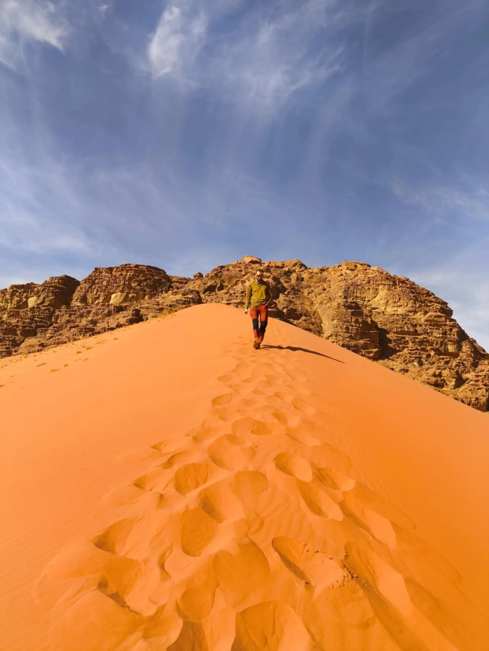 A single line of footprints climbing a red sand dune in Wadi Rum