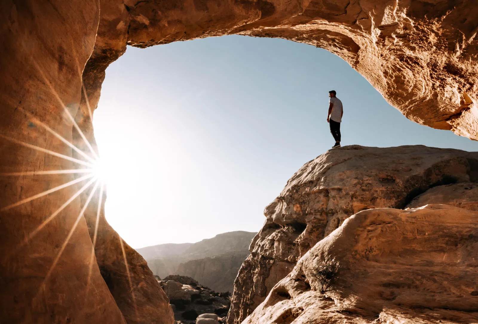 A walker silhouetted in a sandstone arch in Wadi Rum against the sun