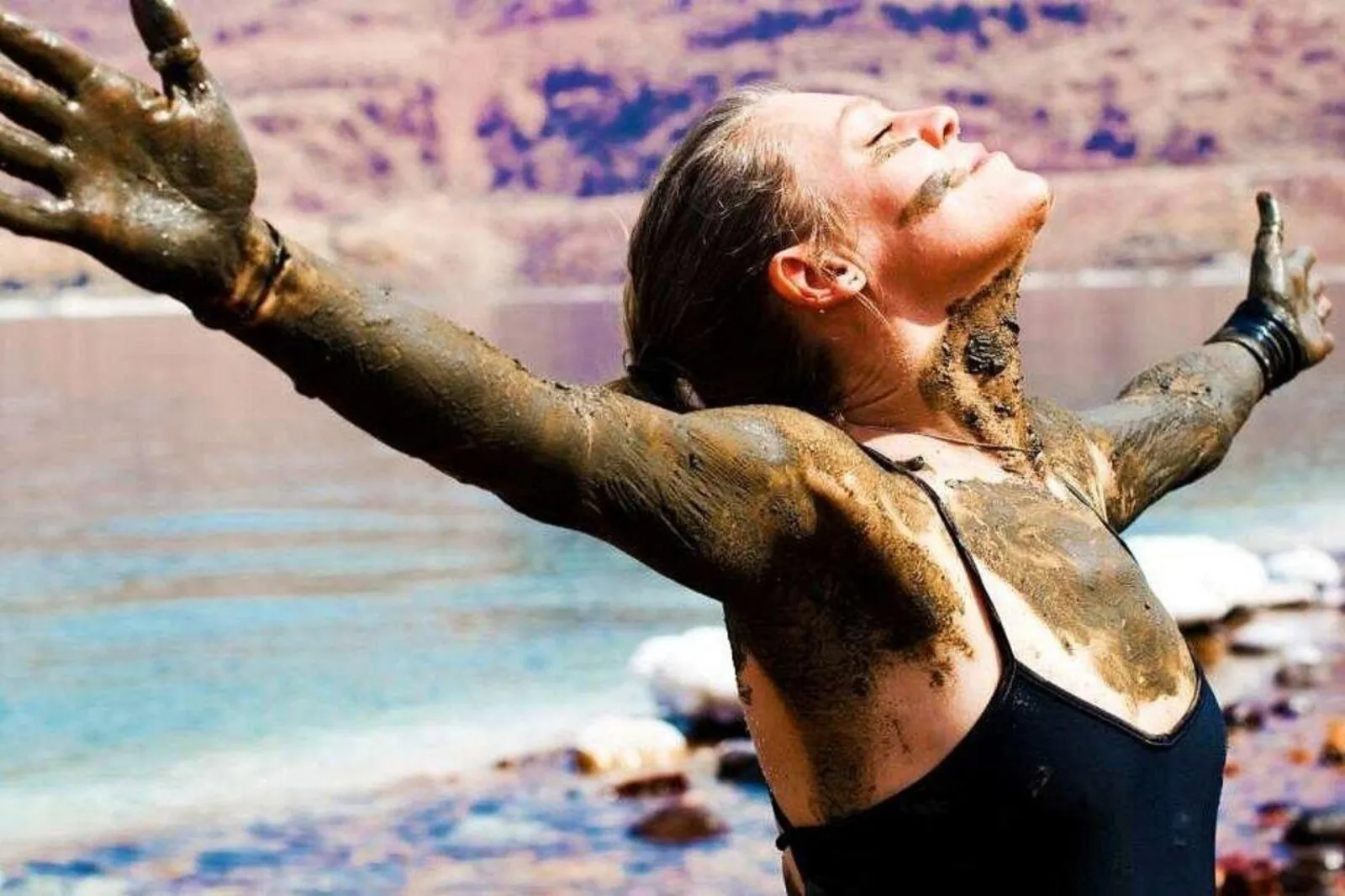 A swimmer coated in Dead Sea mineral mud with her arms spread