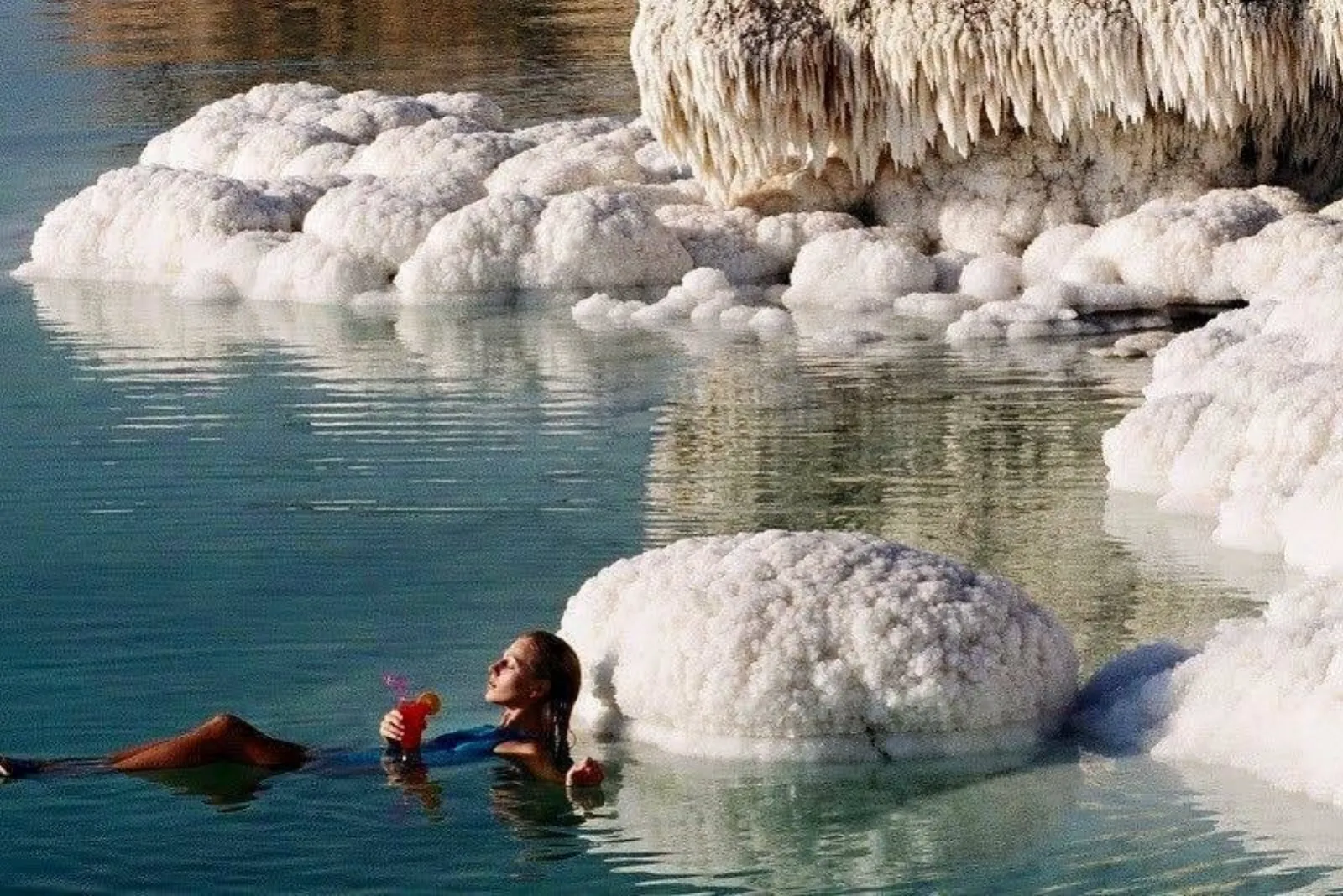 A bather resting against knobbly salt formations in the Dead Sea shallows